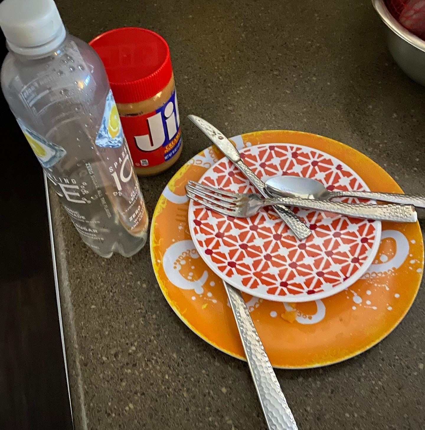 two dirty dishes and utensils plus empty water bottle and jar of peanut butter