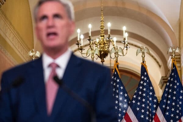 Speaker Kevin McCarthy wearing a blue suit and standing in front of three American flags.