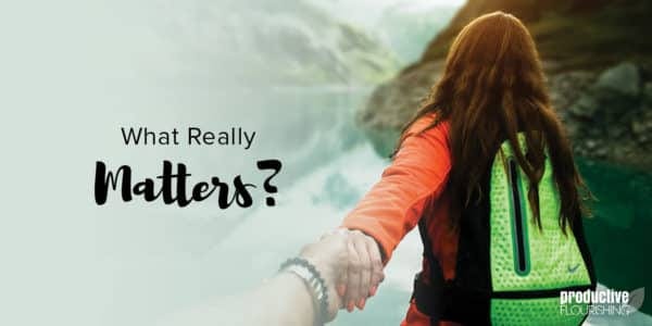 A woman with long dark hair faces away from the camera, holding on to the person behind her, as they walk near water. Text Overlay: What Really Matters?