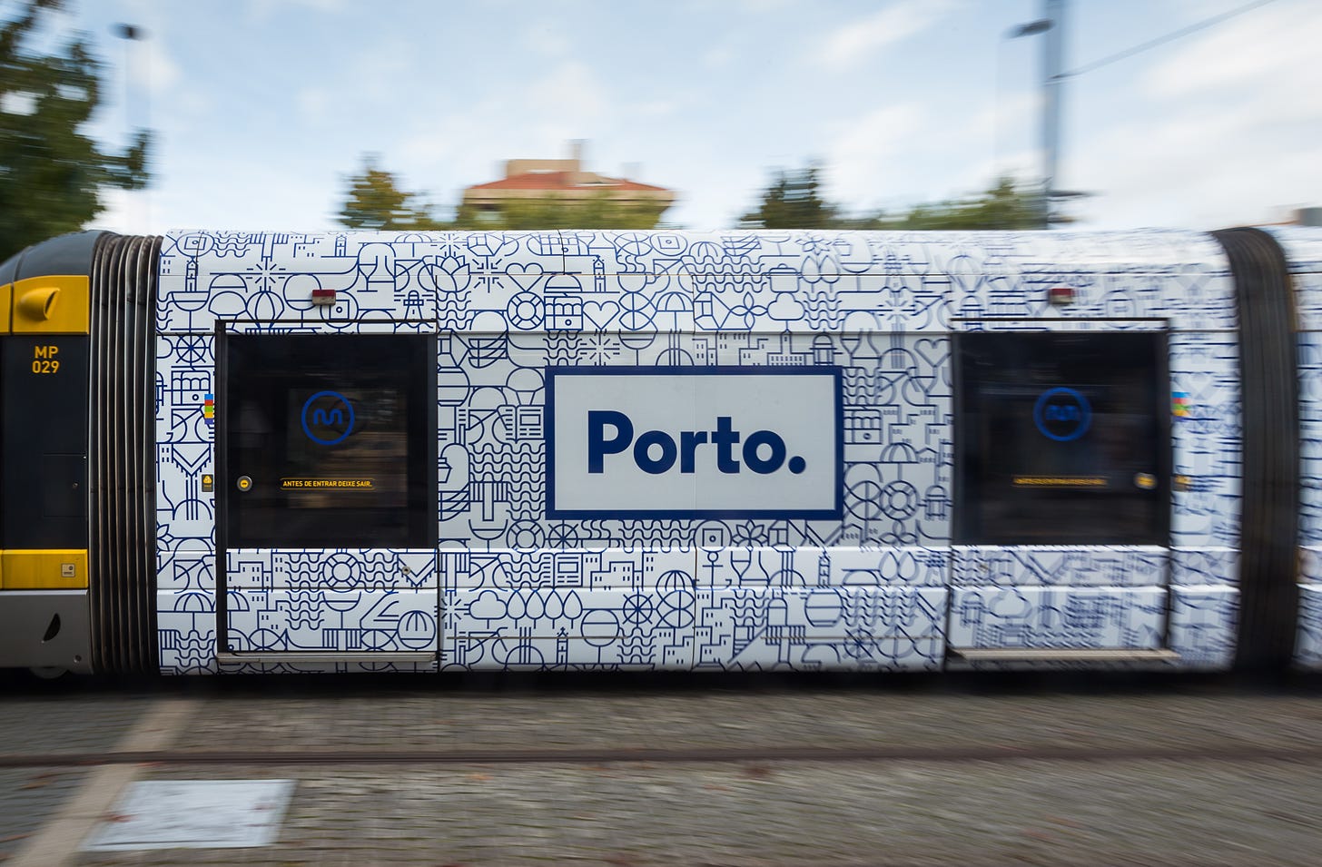 Le porte di un treno urbano di Porto che sfrecciano in città: sulla portiera decorata con i simboli stilizzati della città, campeggia il logo azzurro dentro riquadro bianco: Porto.