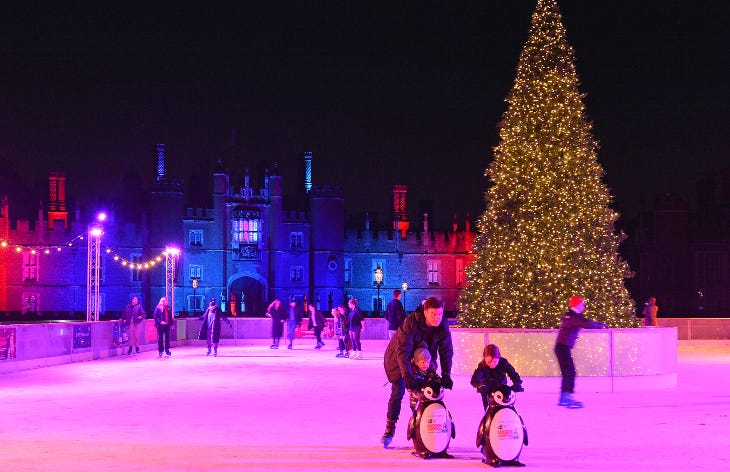 People ice skating alongside a Christmas tree in front of Hampton Court Palace