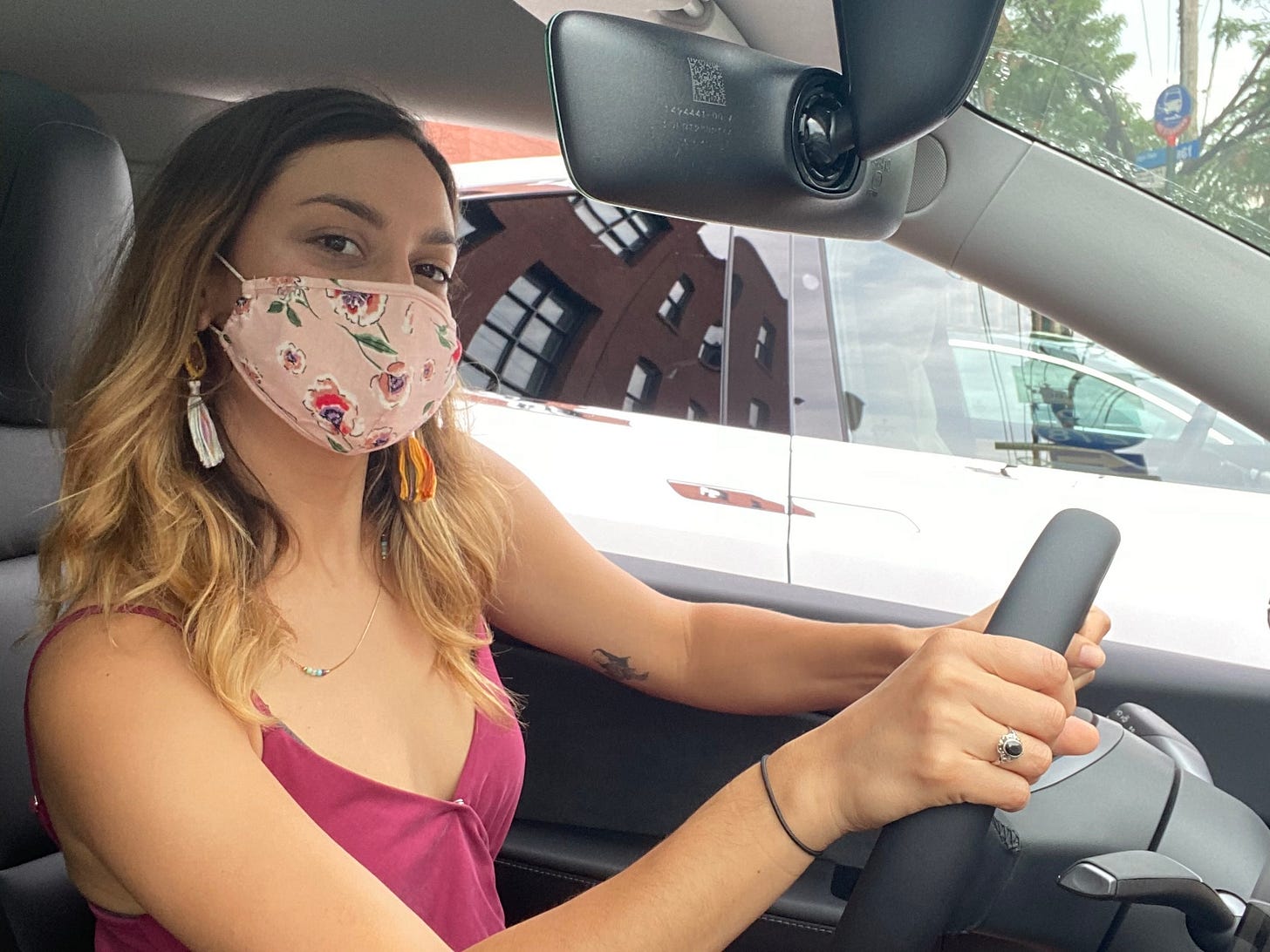 sammi labue wearing face mask sitting behind wheel of a Tesla electric vehicle