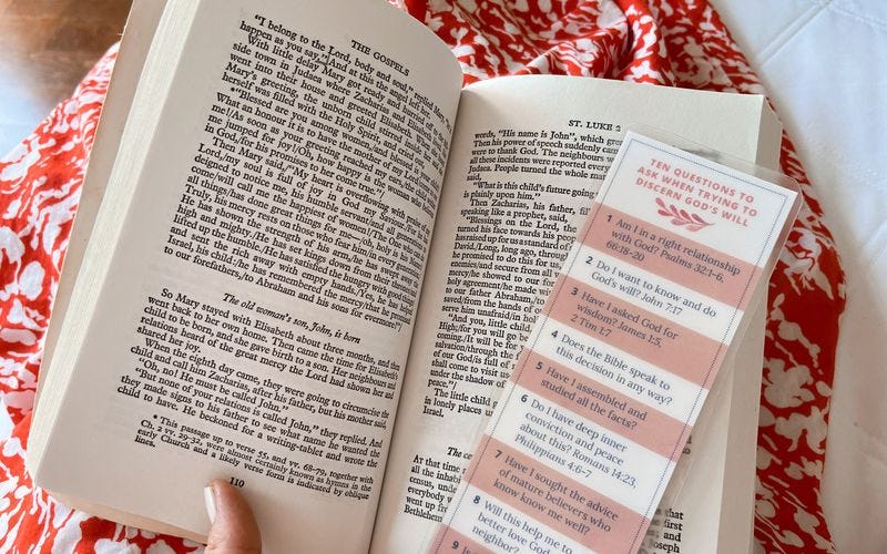 Woman holding a Bible open in her lap with a bookmark titled "10 Questions to Ask When Trying to Discern God's Will"