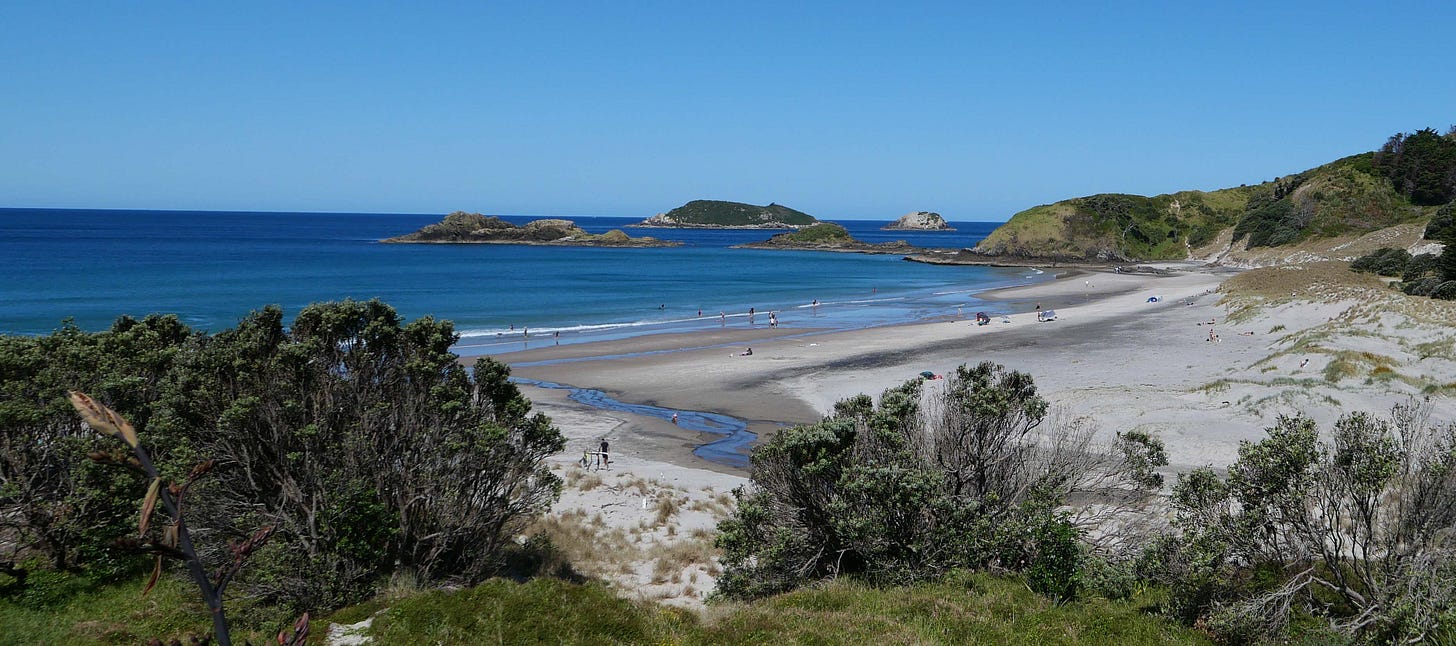 Ocean Beach - white sand leading to a calm, deep blue sea. Several small islands. A clear blue sky.