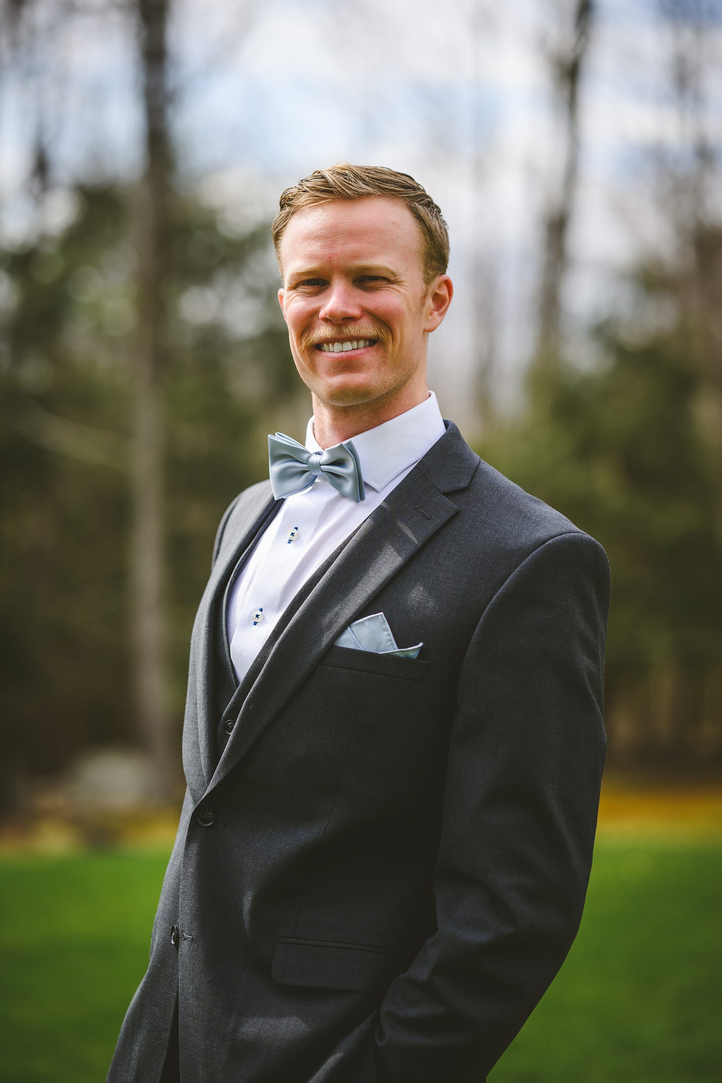 A groom in his suit standing in the woods