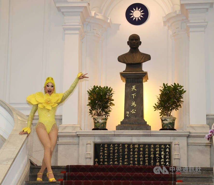 Nymphia Wind, dressed in a bright yellow leotard with a matching yellow wig, performs on a staircase in front of a bust of Sun Yat-sen and a small KMT flag Nymphia Wind, dressed in a bright yellow leotard with a matching yellow wig, performs on a staircase in front of a bust of Sun Yat-sen and a small KMT flag