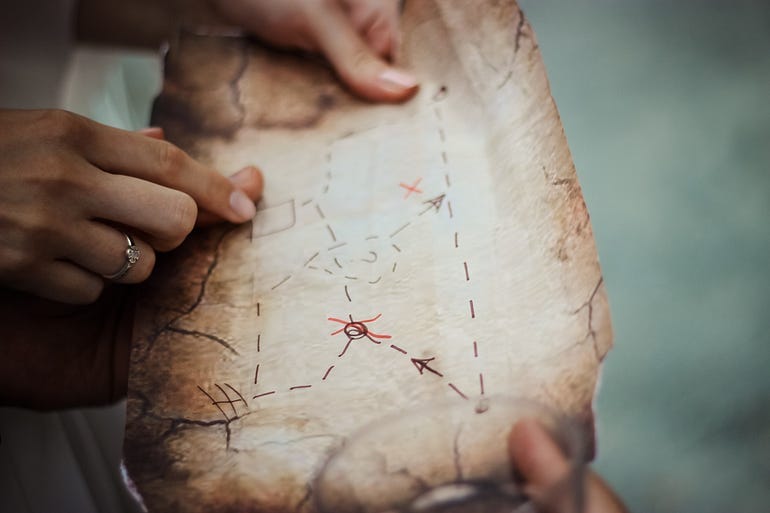 Two hands holding a map that is tracing out a specific route on paper. There are dotted lines that suggest a path, but certain things are “X”ed out