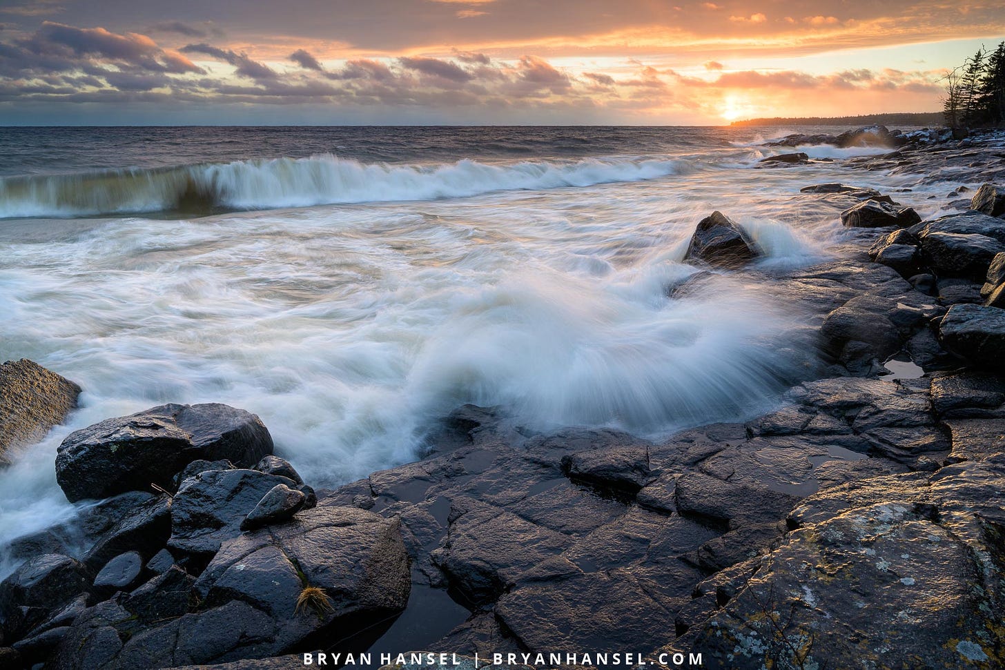 A wave washing up on basalt at sunset.