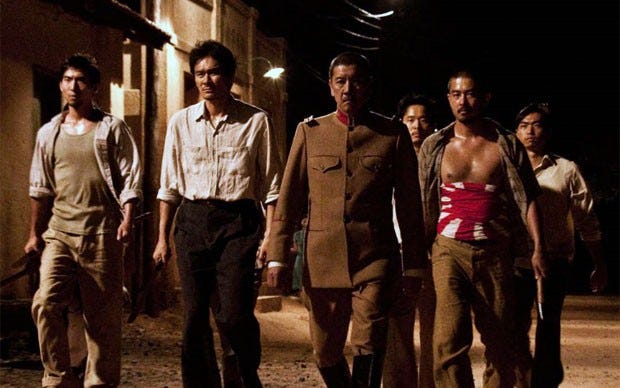 Cena do filme "Corações Sujos" em que 6 homens japoneses armados caminham por uma rua deserta.
