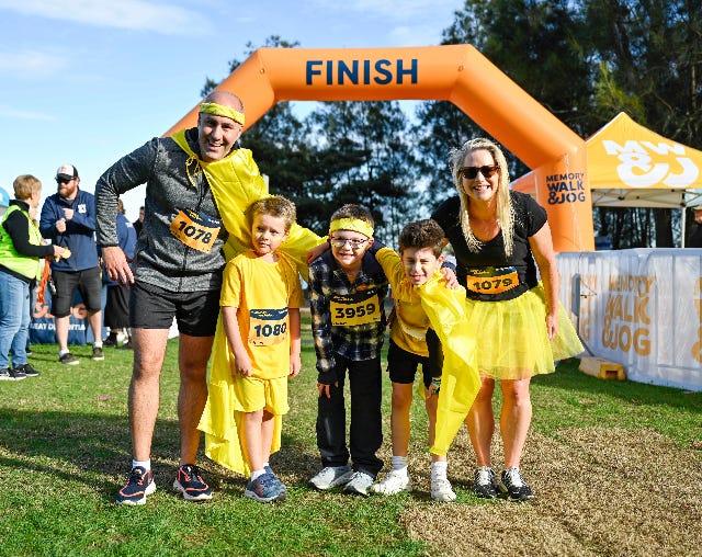 Memory Walk & Jog. Family of two adults and three young children standing at the finish line.