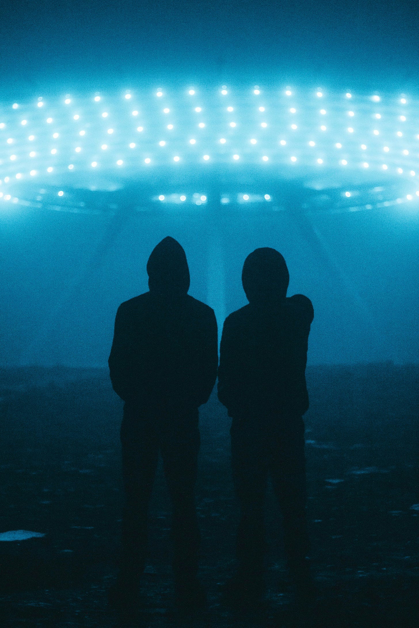 Two silhouettes of people in hoods stand before a  lit up flying saucer