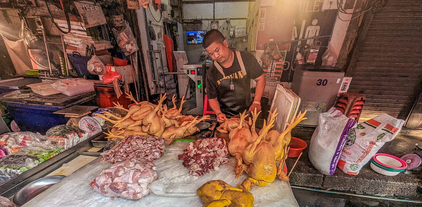 A man in an apron cutting up chicken carcasses. 