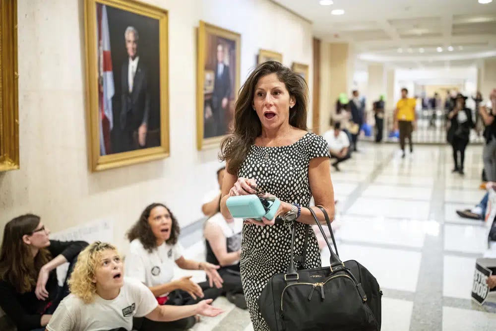 Laura DiBella, the Florida state secretary of commerce, walks past dozens of activists in shock as they chant "Where is Ron," as part of a sit-in outside Florida Gov. Ron DeSantis' office, Wednesday, May 3, 2023, in Tallahassee, Fla. (Alicia Devine/Tallahassee Democrat via AP)