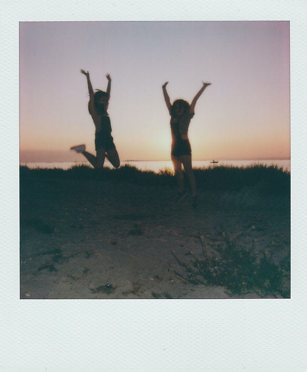 Poloroid image of two women on the beach at sunset jumping in joy.