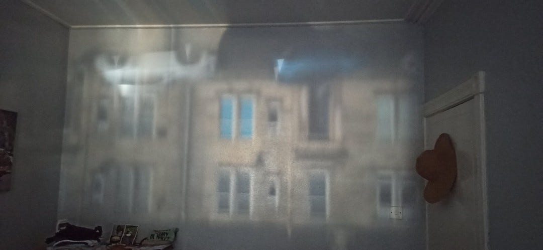 The camera obscura effect of the row of houses opposite my apartment lit by sunlight and shining on my bedroom wall through a tiny gap in my curtains, showing me an inverted, live-streaming view of the whole street.