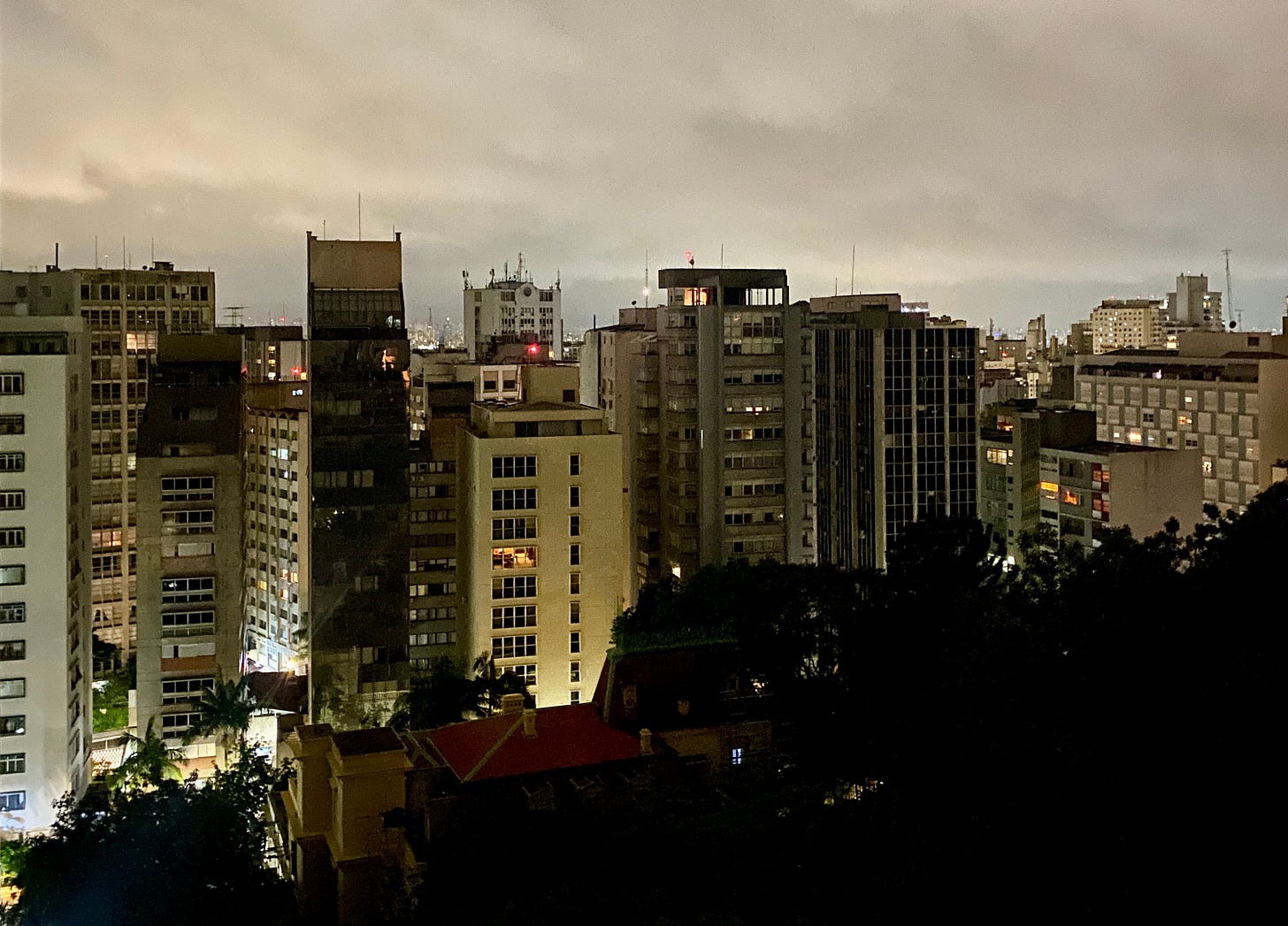 Foto de São Paulo à noite, com uma área verde na frente e na frente dela, uma fileira de prédios 