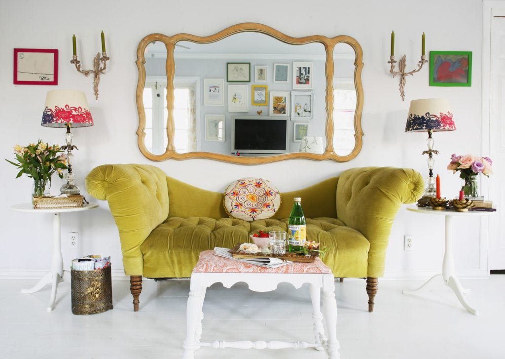 Bright green velvet sofa in an all white room with colourful, eclectic furnishings and accessories. 