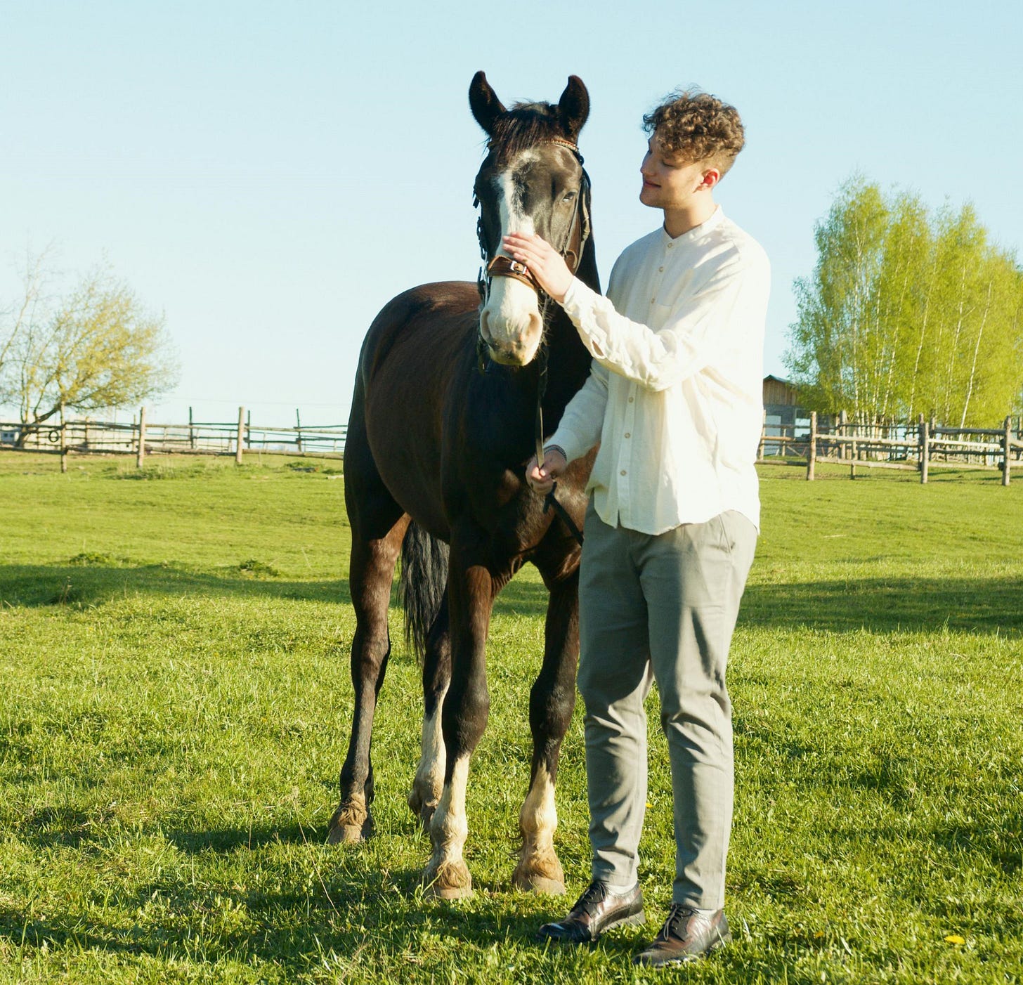 Young man standing by horse, holding lead in one hand and patting her nose.