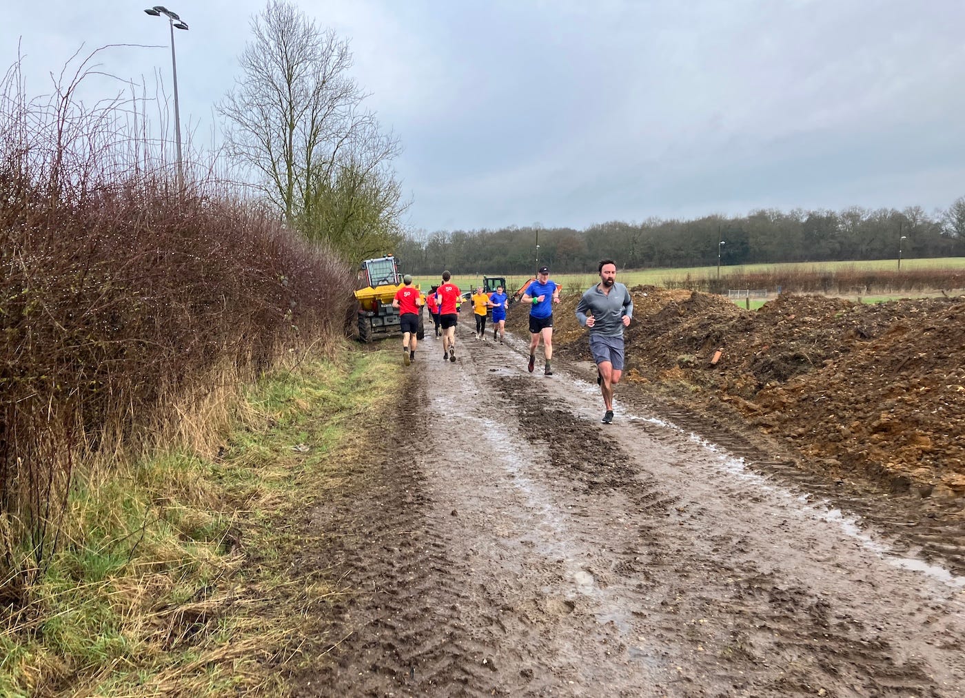 Runners on both sides of a muddy path with tractor tracks.