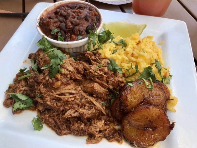 plate of pork shoulder, rice and beans, and candied plantains. Topped with fresh cilantro and served with a wedge of lime.