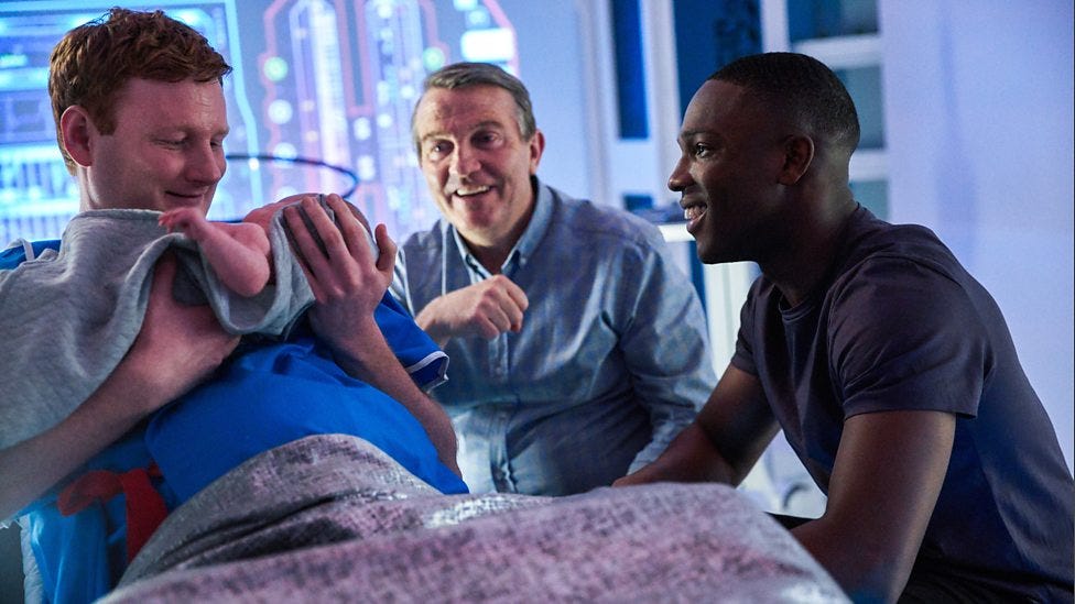 This image from "The Tsuranga Conundrum" (Doctor Who Series 11's fifth episode) shows the character of Yoss (played by Jack Shalloo, left), a male Gifftan, holding his just-born baby while Graham O'Brien (played by Bradley Walsh, center) and Ryan Sinclair (played by Tosin Cole, left) sit next to Yoss. All three characters smile at the baby. This image from "The Tsuranga Conundrum" (Doctor Who Series 11's fifth episode) shows the character of Yoss (played by Jack Shalloo, left), a male Gifftan, holding his just-born baby while Graham O'Brien (played by Bradley Walsh, center) and Ryan Sinclair (played by Tosin Cole, left) sit next to Yoss. All three characters smile at the baby.