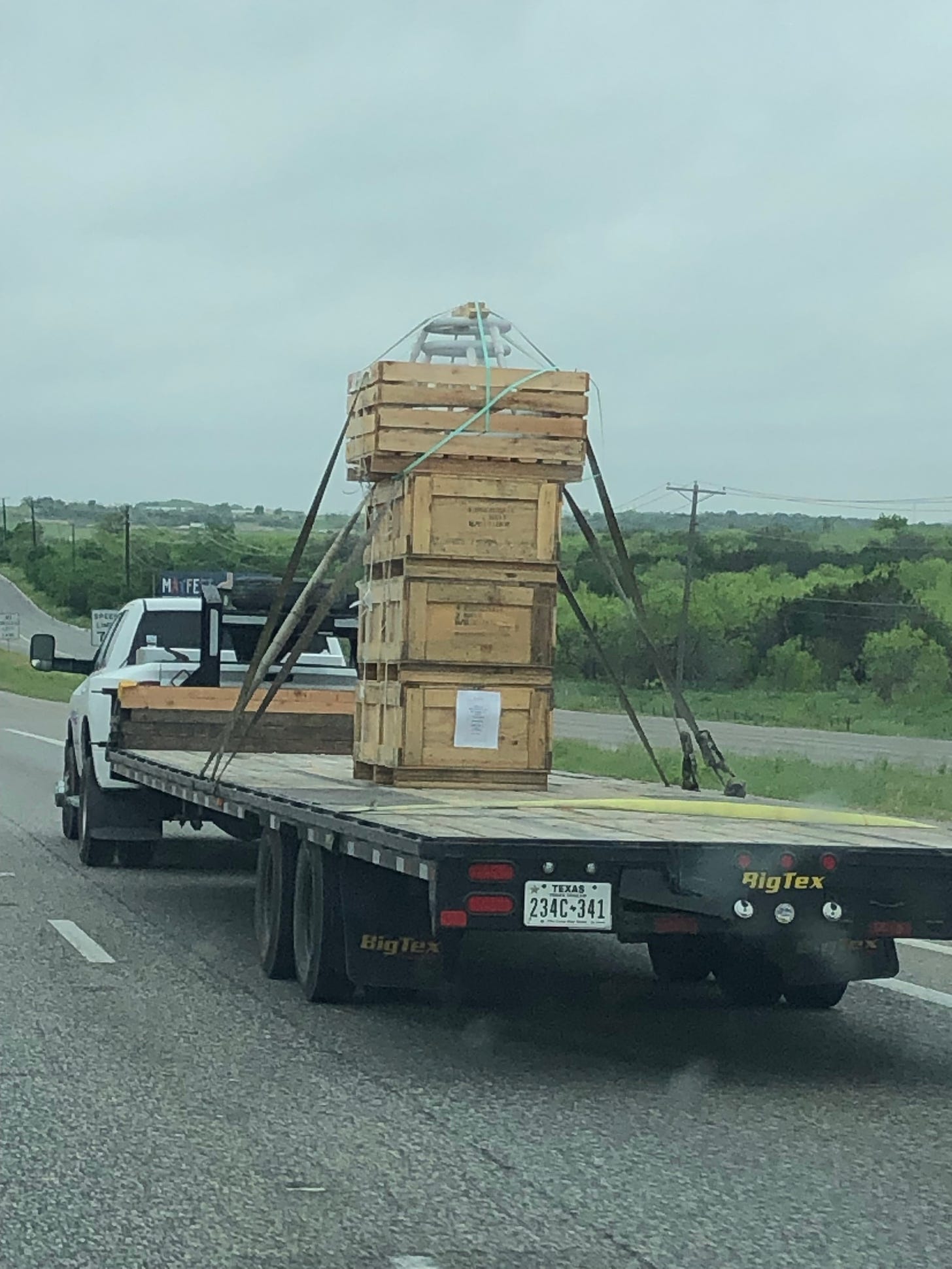 A flatbed truck with wooden crates stacked in a single pile, strapped down on a flatbed truck, looking very precarious