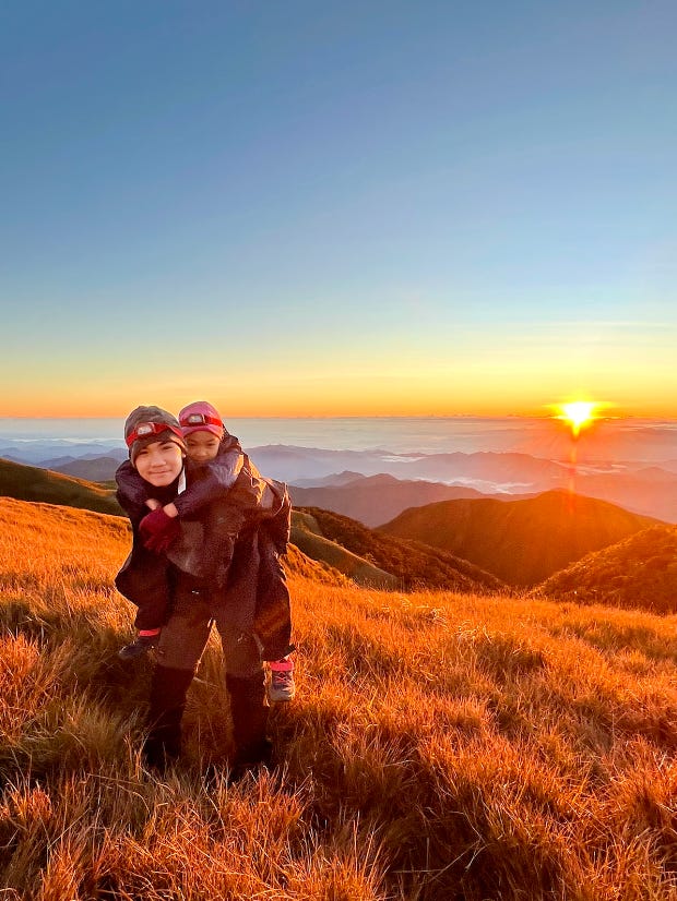 Teenage boy carrying a little girl against the backdrop of an orange sunrise, mountains and a sea of clouds