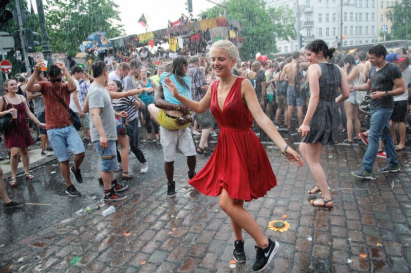 Young woman in a red dress dances in the middle of a crowd on a Berlin street.