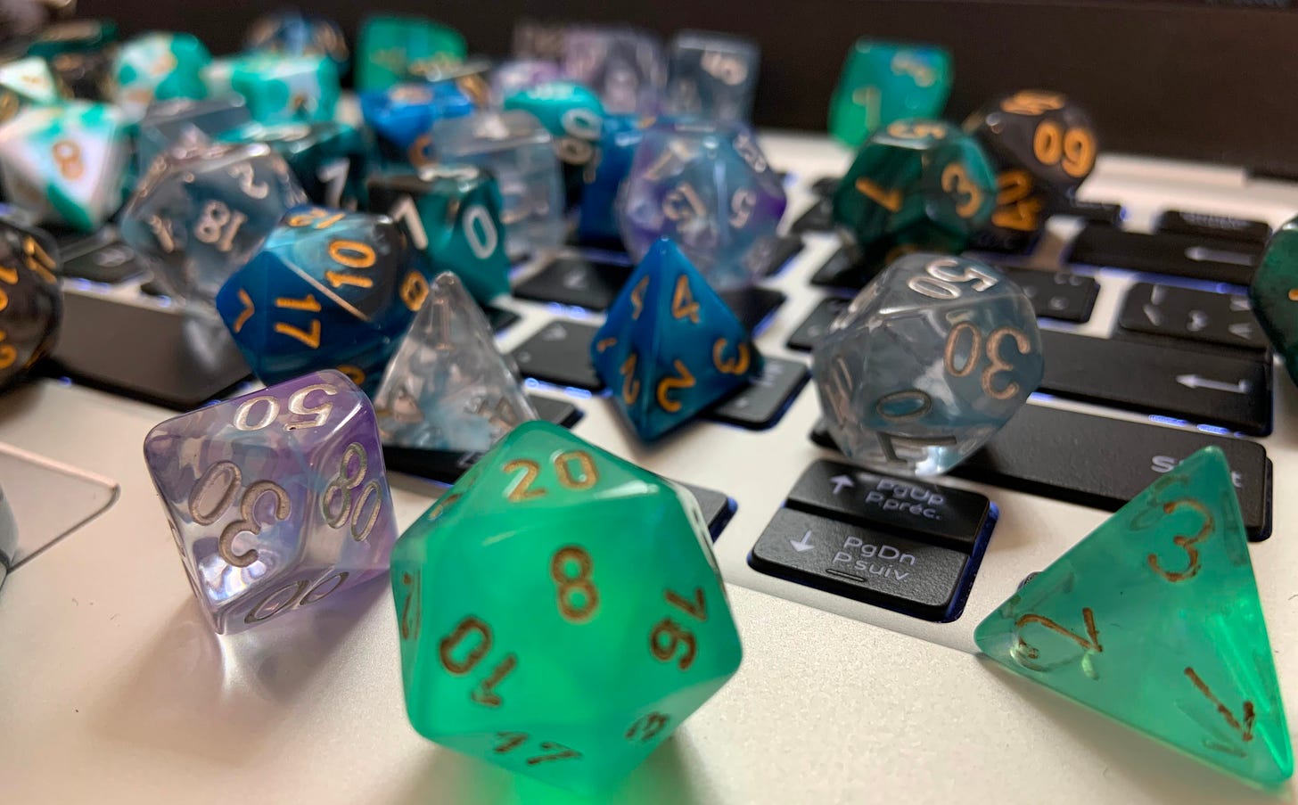 A selection of blue and green polyhedral dice scattered across a laptop keyboard.