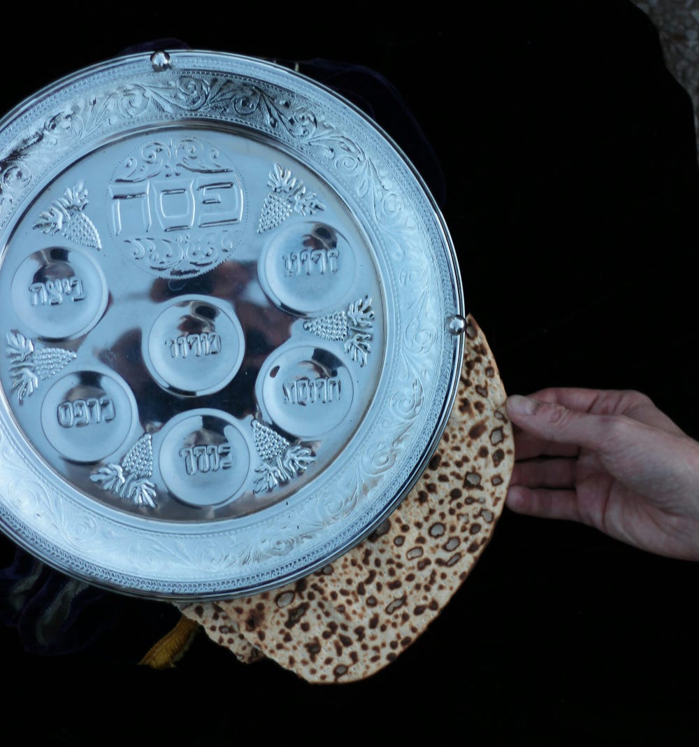 Silver seder plate with someone putting matzo in the compartment below it
