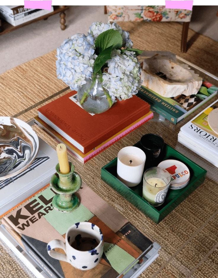 This may contain: a coffee table topped with books and vase filled with flowers next to a candle holder