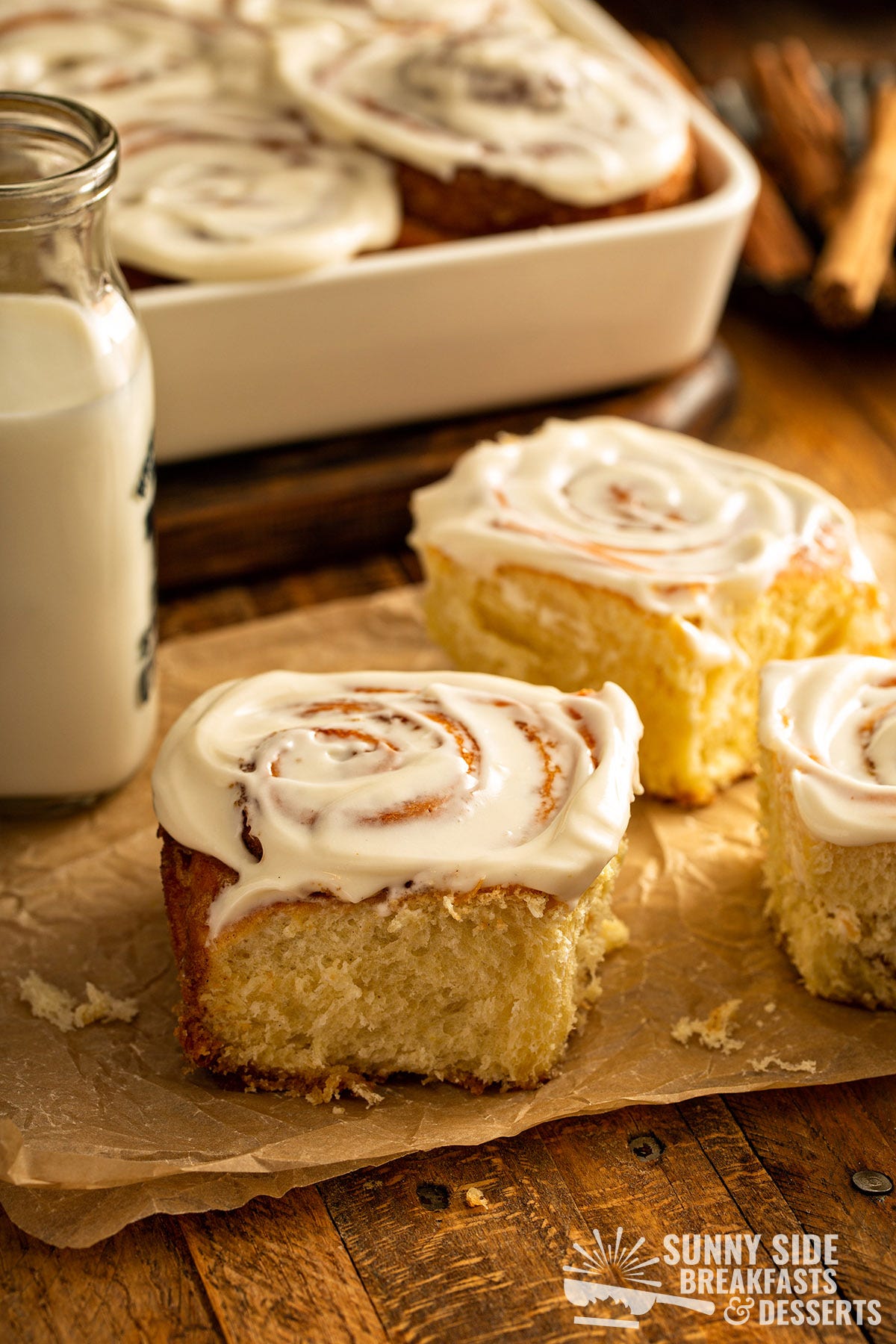 Frosted cinnamon buns next to a jar of milk.