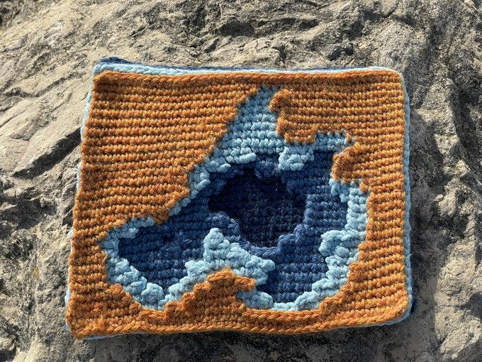 A small crocheted square comprises of four superimposed layers representing depth contours for Lake Mendota. The top orange layer represents the land, and each blue layer underneath represents a deeper part of the lake.
