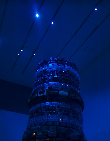 The top half of Babel by Cildo Meireles: a circular stack of radios under a deep blue light. Some of the radios have red and yellow lights on them.