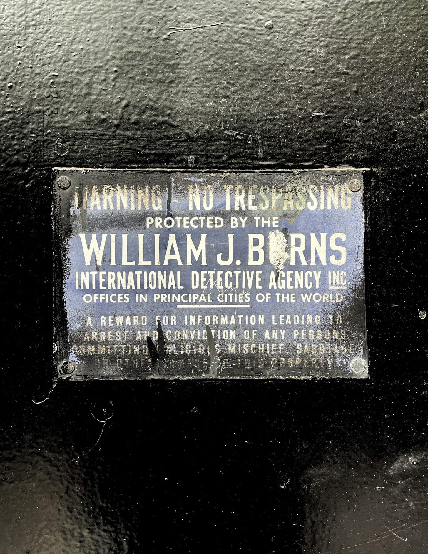 A black and white sign reading Warning- No Trespassing. Protected by William J. Burns