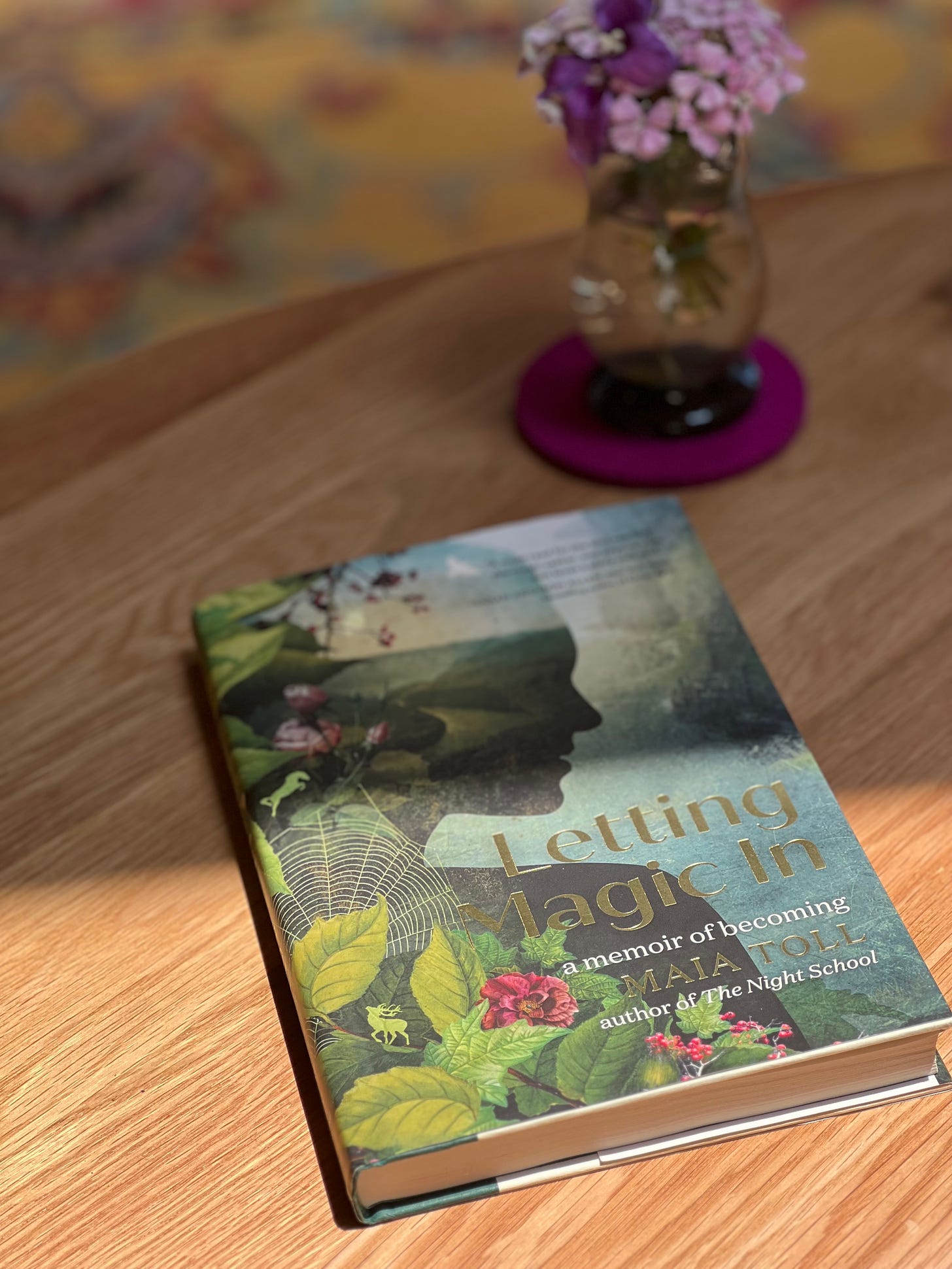 Copy of Letting Magic In book on a coffee table next to purple flowers