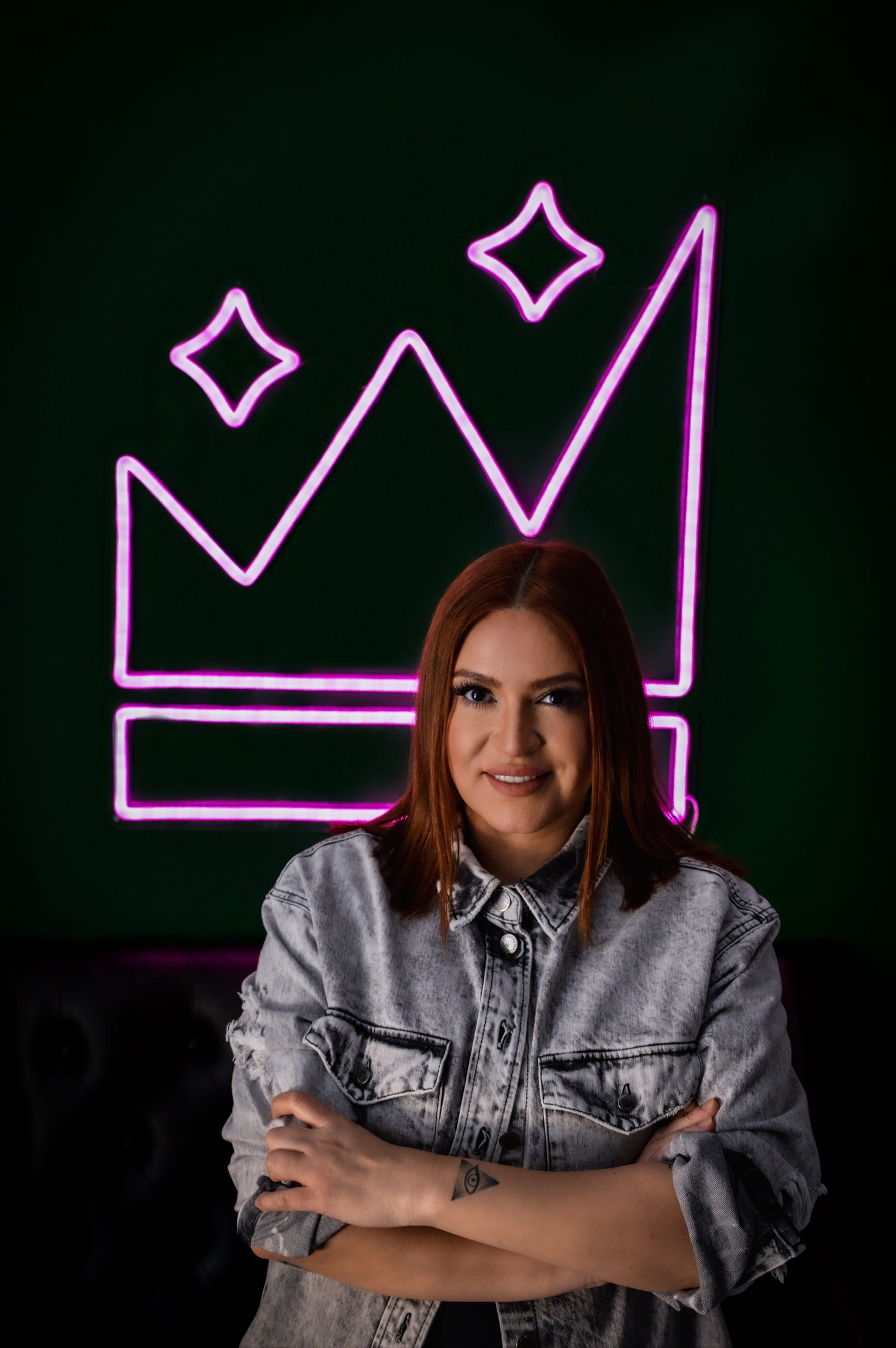 Linda Garcia in a denim jacket in front of a bright pink neon crown