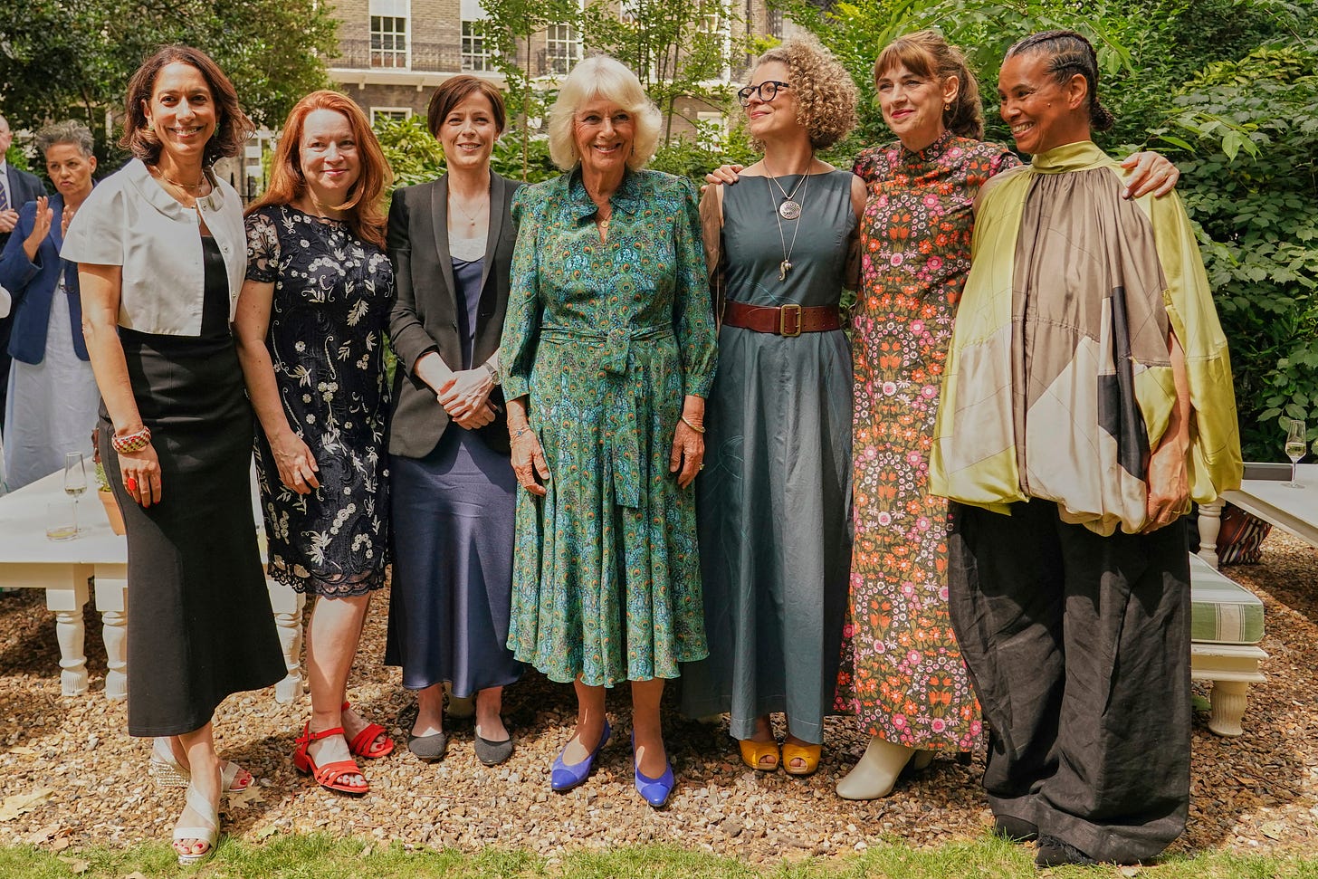 Queen Camilla wearing peacock print dress and standing with female authors