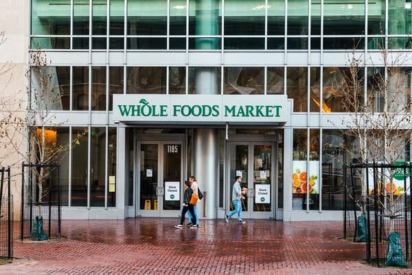 A glass and steel building with a sign that states “Whole Foods Market” above a doorway. The doors have signs that state “Store Closed.”
