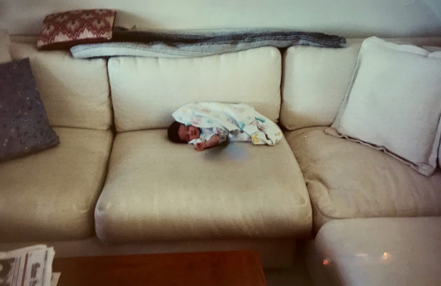 Infant with black hair wrapped in blanket on a huge beige sofa