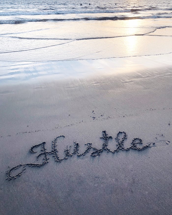 The word ‘Hustle’ written in sand at the beach. The word ‘Hustle’ written in sand at the beach.