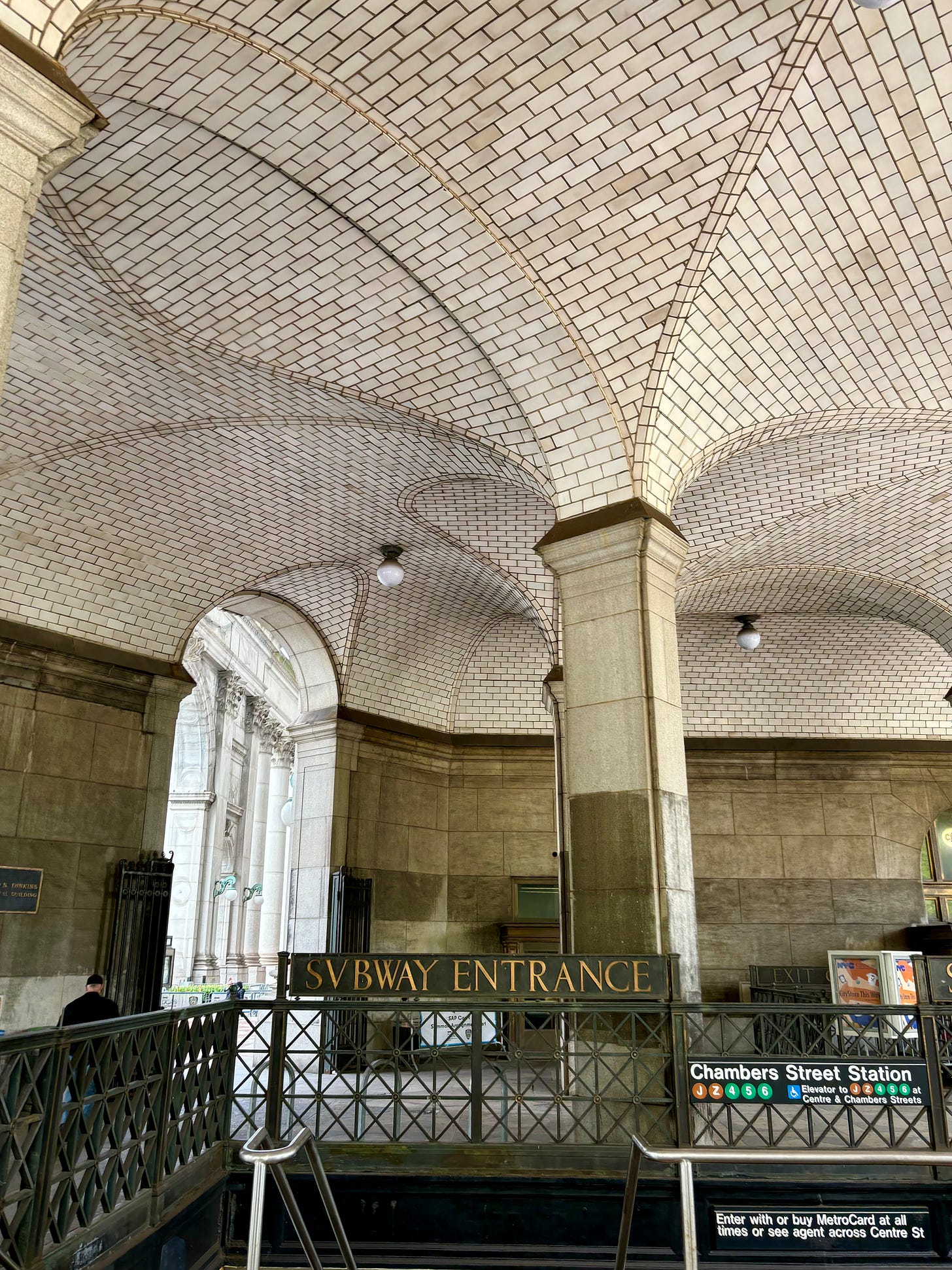The Municipal Building entrance of the Chambers Street Station. The ceiling is high and graceful, a series of arches in elegant white tile.