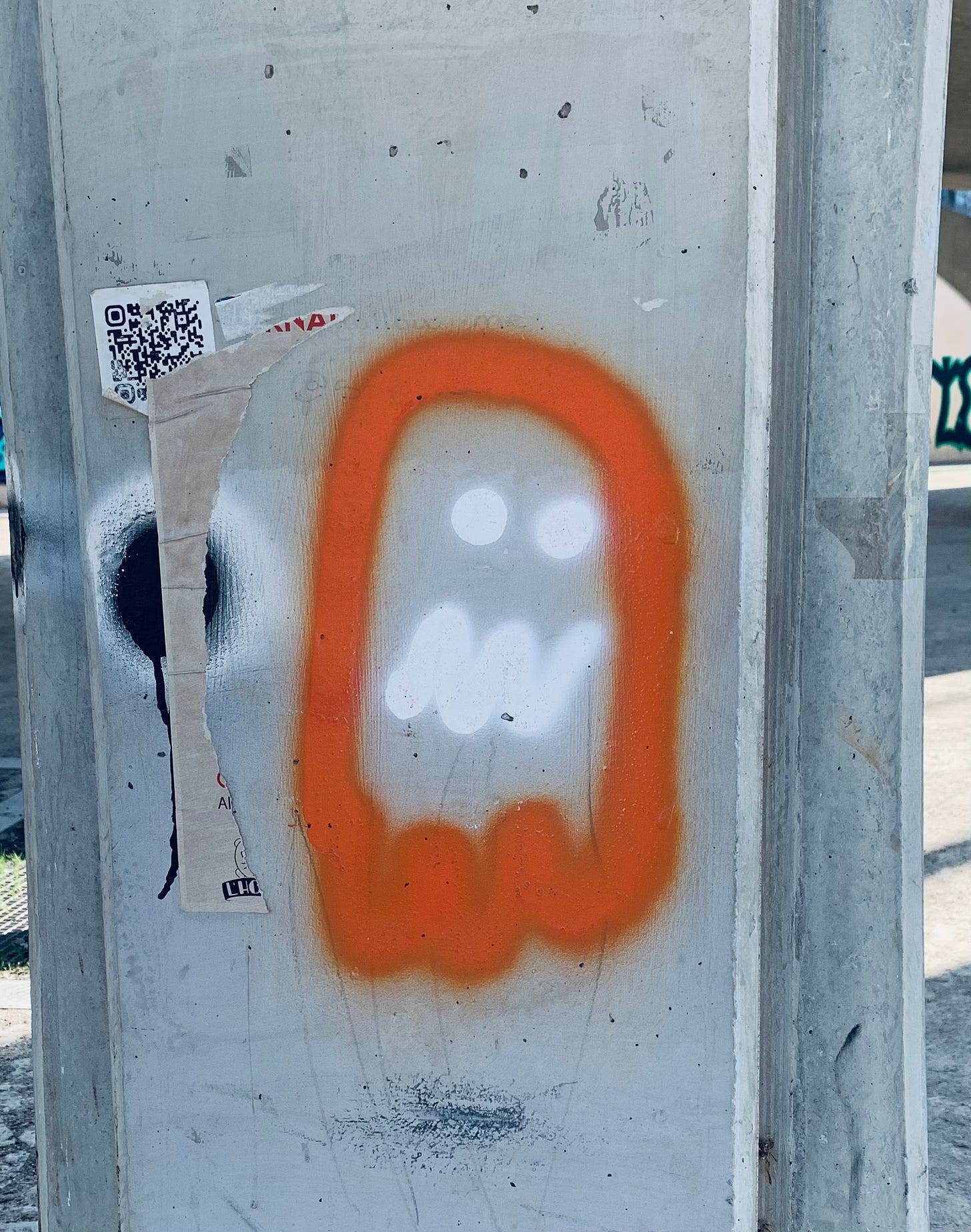 An orange and white ghost in the style of the Pac-Man video game is spray painted on a concrete pillar in the Turia.