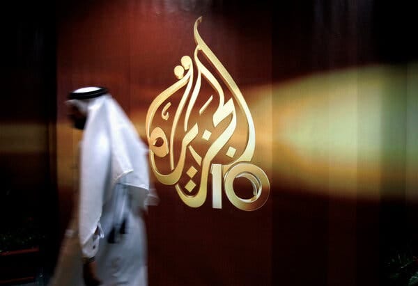 A person walking past the logo of Al-Jazeera.