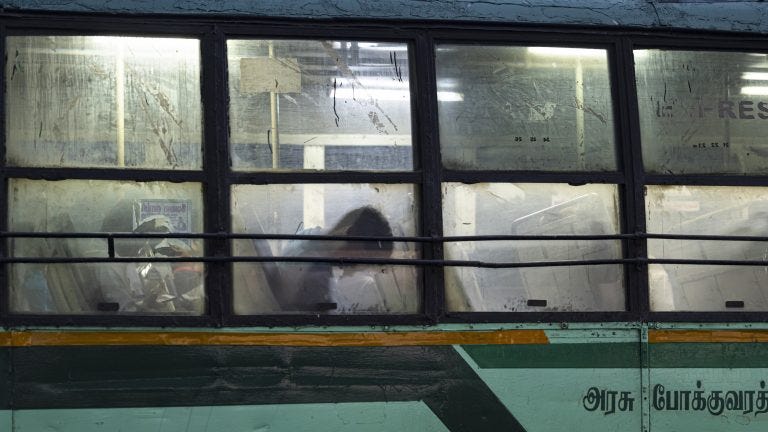 A photo showing the exterior of a bus at night with a silhouette of a person's head slumped against the window.