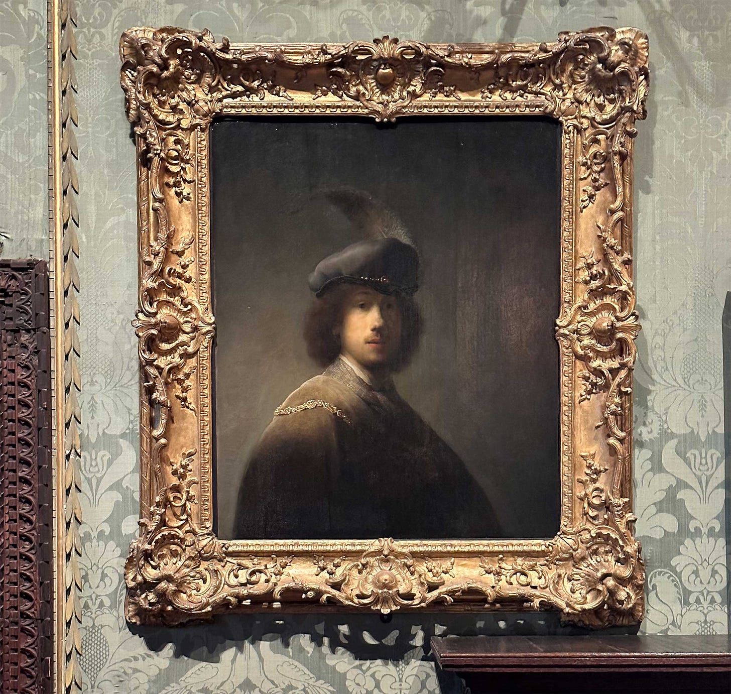 Self portrait of a young Rembrandt against a dark background, wearing a hat with a feather.