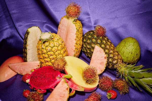 A spread of carved open pineapples, mangoes, rambutans and other fruits on a purple silk backdrop.