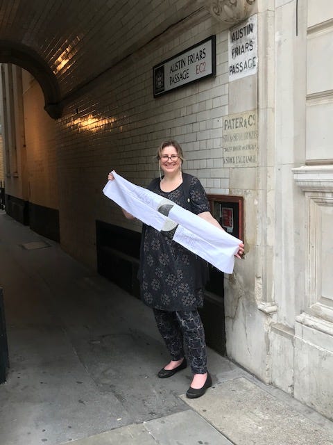 A white woman holds fabric up in an alleyway that is signposted Austin Friars Passage