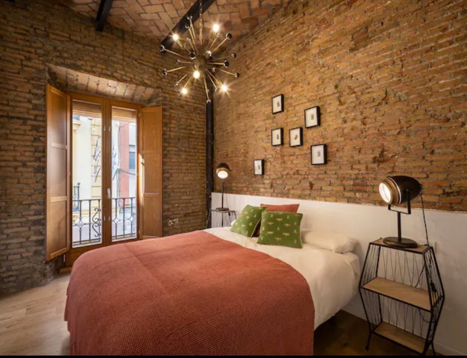 An apartment bedroom with exposed brick walls and a balcony