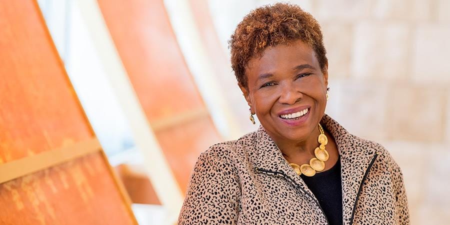 A photo of Dr. Barbara Holmes smiling at the camera in front of an orange background.